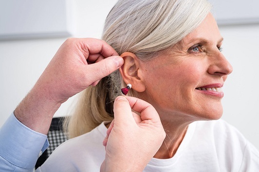 Ältere Frau bekommt ein modernes Hörgerät angepasst und lächelt zufrieden im Hörakustikerstudio.